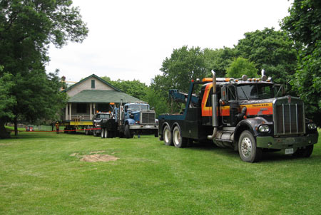 three trucks pull the trailer-mounted house