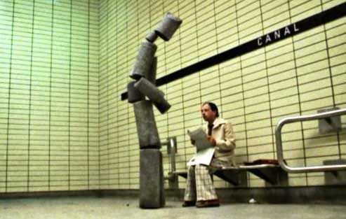a humanoid made of chunks of concrete post stands over a worried looking man